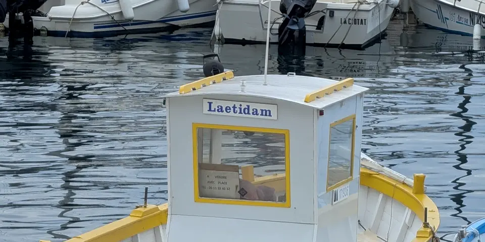 Ein kleines weiß-gelbes Boot liegt vertäut an einer Kaimauer im ruhigen Hafenbecken.
